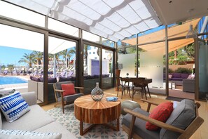 Un área de estar moderna con vista a la piscina, con asientos cómodos y una mesa redonda de madera.