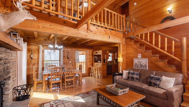 Eine geräumige Holzdiele mit Essbereich, einem Wohnzimmer mit Sofa und Kamin sowie einer Treppe zu einer oberen Ebene.