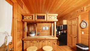 Eine Holz-Küche mit Barbereich, zwei Barhocker, einem Kühlschrank und einer Uhr an der Wand.