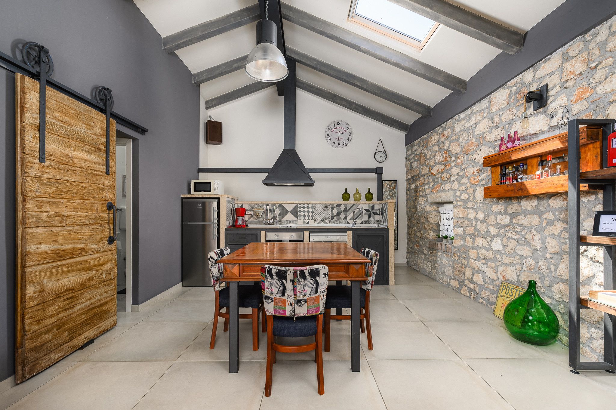 A modern kitchen with a dining area, featuring a wooden table, chairs, and a stone wall.