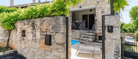 A stone building with a pool, outdoor seating, and a gate.