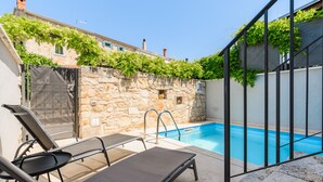 A pool area with a stone wall, a metal gate, and a lounge chair.