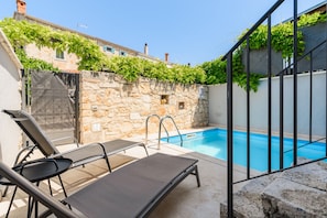 Un espace piscine agrémenté d’un mur en pierre, d’une porte en métal et d’une chaise longue.