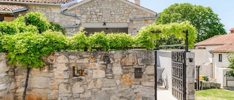 A stone wall with a gate, a clear sky, and a building with a tiled roof.