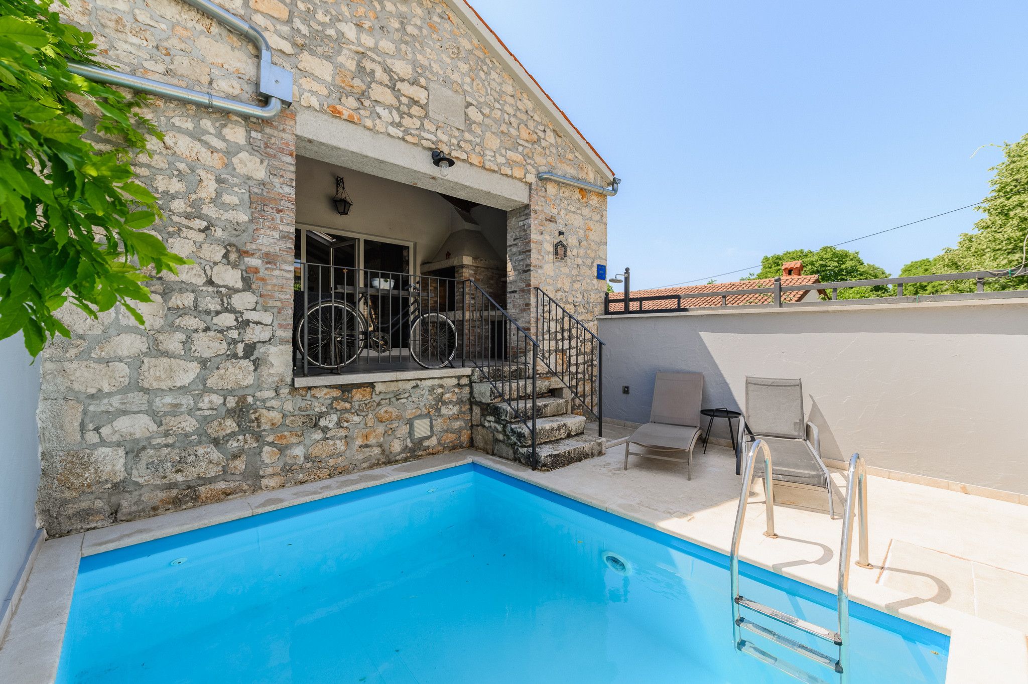 A stone building with a swimming pool, outdoor seating, and a bicycle.