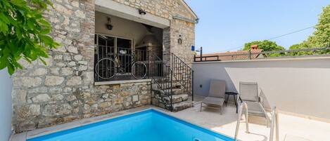 A stone building with a swimming pool, outdoor seating, and a bicycle.