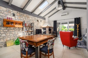 Ein Essbereich mit Holztisch und Stühlen, einer Steinwand, einem Kamin und Blick ins Freie.