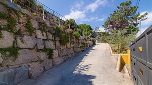 A narrow, paved pathway flanked by a stone wall with vegetation on one side and a yellow barrier on the other. - Club Villamar - Modern, spaciously designed holiday villa that can accommodate 17 people, with pr... (Lloret de Mar)