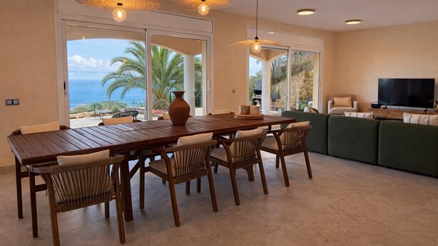 A spacious living area with a wooden dining table, wicker chairs, a green sofa, and a flat-screen TV. - Club Villamar - Modern, spaciously designed holiday villa that can accommodate 17 people, with pr... (Lloret de Mar)