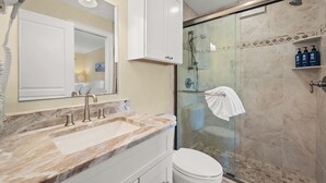 Une salle de bain avec un lavabo en marbre, des toilettes, une douche en verre et un miroir avec éclairage intégré.