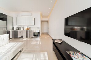 A modern kitchen with white cabinets, a black countertop, and a large flat-screen TV.