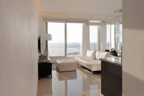 A modern living room with a large window, a sofa, a small table, and a lamp.