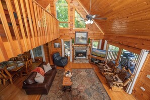 A wooden cabin interior with a dining area, living room, fireplace, and a balcony with a view of the outdoors. - Private Mountain Views! Pool Table, Hot Tub, Arcade Game, Pool/Putt Putt/Fishing (Sevierville)