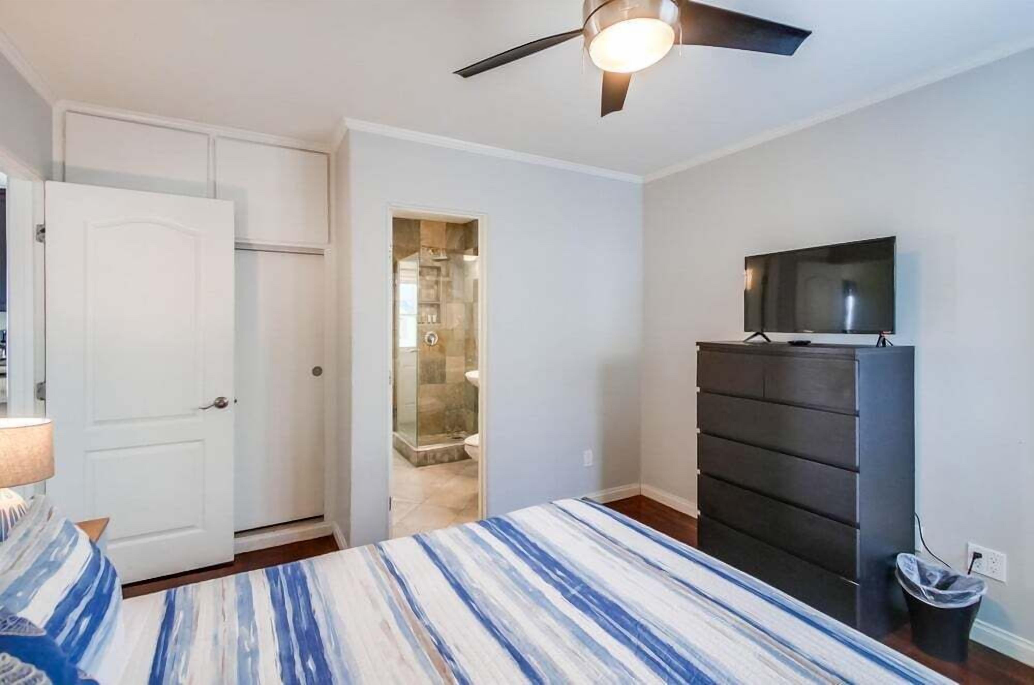 Ein Schlafzimmer mit Bett, Kommode, Fernseher und Deckenventilator.