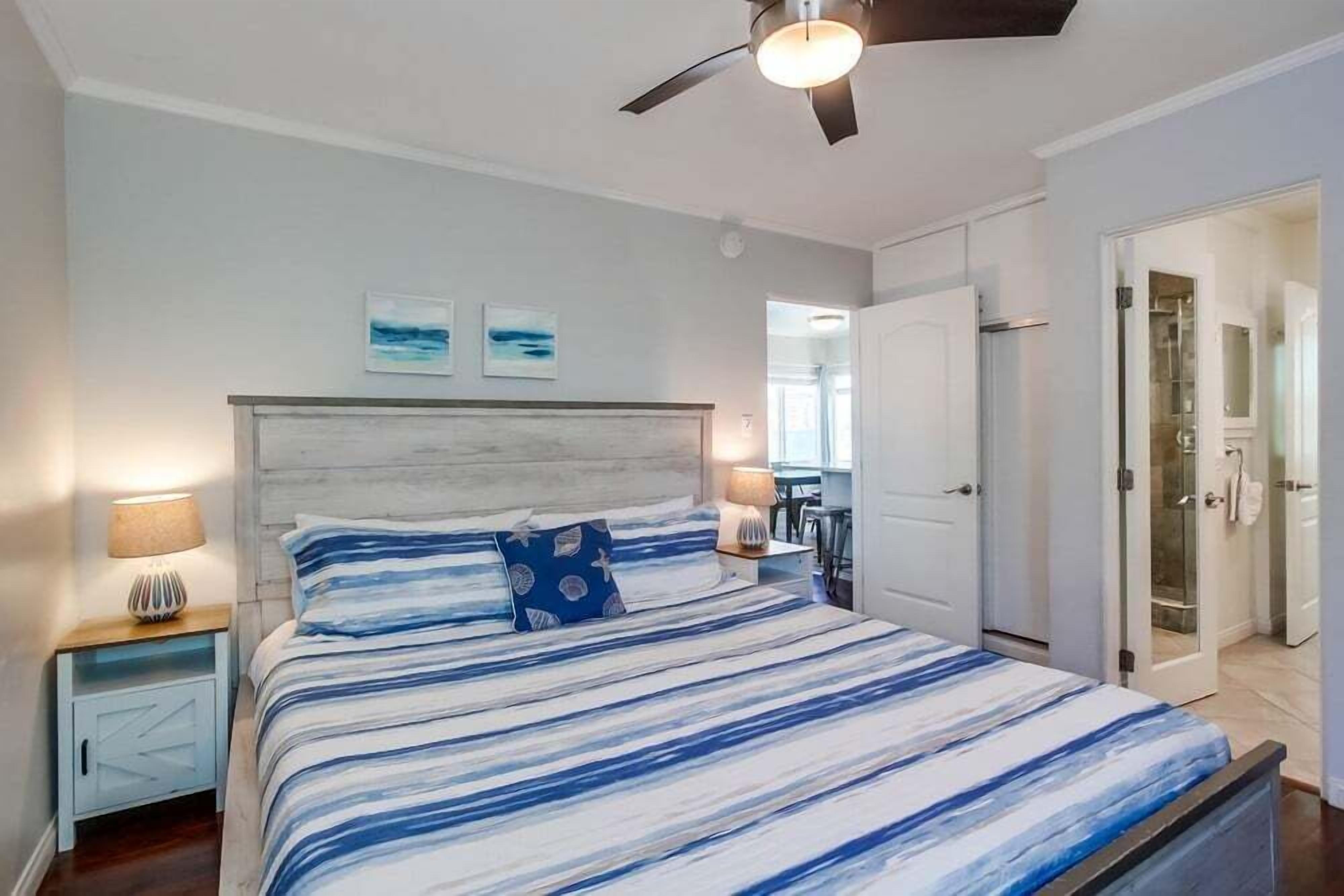 A bedroom with a bed, nightstands, a ceiling fan, and a door leading to a bathroom.