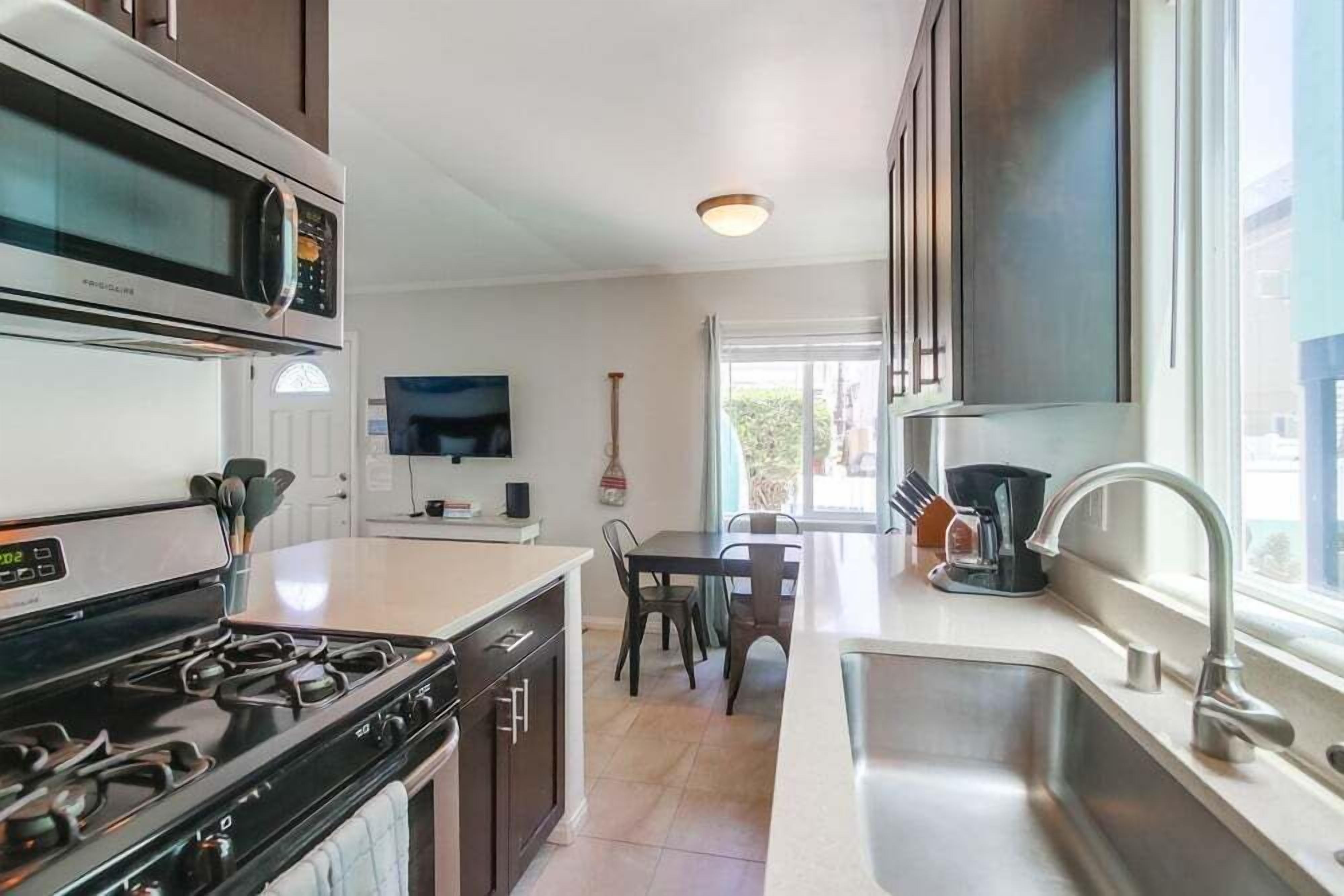 Una cocina moderna con microondas, estufa y lavaplatos. Hay un comedor con mesa y sillas.