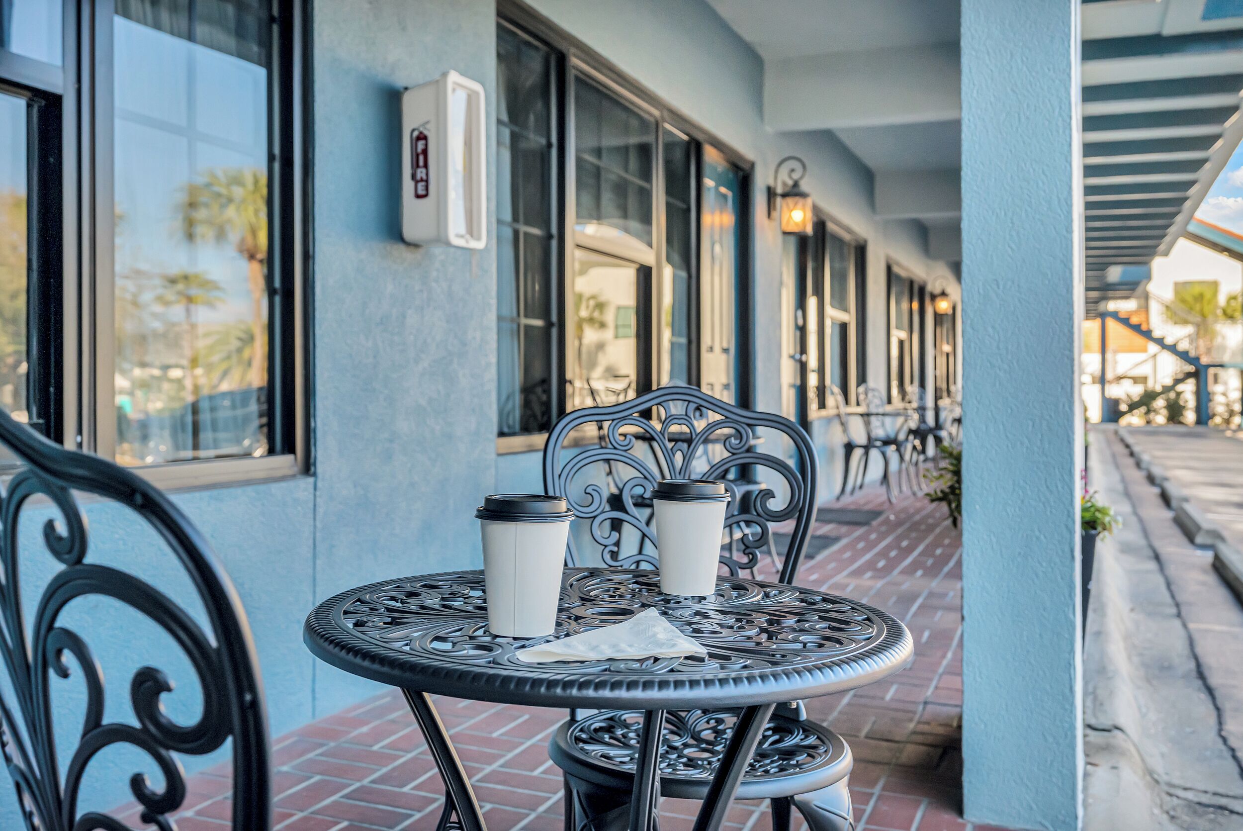 A metal table with two coffee cups and a napkin on a patio with brick flooring.