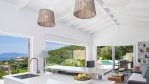 A modern kitchen with a large island, a dining area with a view of the sea, and a living room with a pool view. - Villa Koumaria - Secluded Elegance with Amazing Sea Views & Infinity Pool (Sivota)