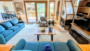 Ein geräumiges Wohnzimmer mit Holzboden, einem großen Fernseher und einem Kamin. In der Mitte befinden sich zwei Sofas und ein Couchtisch.