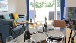 Un coin repas avec une table dressée pour deux personnes, une bouteille de champagne et un téléviseur en arrière-plan.