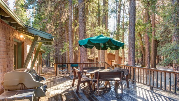 Eine Holzterrasse mit Sitzgelegenheit, Grill und Blick auf hohe Bäume.