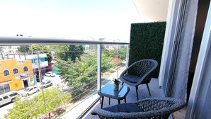 A balcony with wicker chairs and a small table, overlooking a street with buildings and trees.