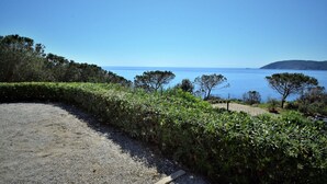 A coastal road with a gravel path, dense greenery, and a clear view of the sea and distant hills. - Scrittore2 - Scrittore2 Villa Fiore (Capoliveri)