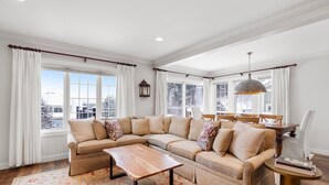 A modern living room with a sectional sofa, a coffee table, and a dining area with a chandelier. - Dog Friendly Resort Home at Topnotch Spa & Resort (Stowe)