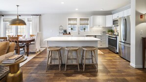 A modern kitchen with a central island, bar stools, and stainless steel appliances. - Dog Friendly Resort Home at Topnotch Spa & Resort (Stowe)