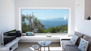 A modern living room with a large window offering a view of the sea and hills. - Villa NISI – Stylish Sea-View Retreat with Pool & Easy Access (sivota)