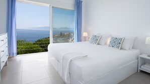 A bedroom with a large bed, a nightstand, a dresser, and a view of the sea through a sliding glass door. - Villa NISI – Stylish Sea-View Retreat with Pool & Easy Access (sivota)