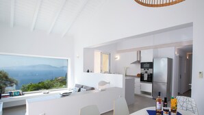 A modern kitchen with a large island, a dining area with a table set for two, and a view of the sea through a large window. - Villa NISI – Stylish Sea-View Retreat with Pool & Easy Access (sivota)