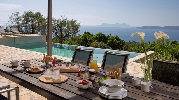 A wooden table with breakfast items and a view of the sea. - Villa NISI – Stylish Sea-View Retreat with Pool & Easy Access (sivota)