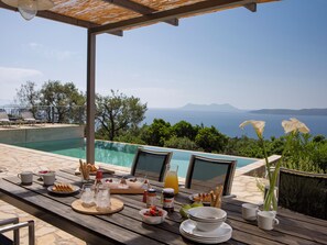 A wooden table with breakfast items and a view of the sea. - Villa NISI – Stylish Sea-View Retreat with Pool & Easy Access (sivota)