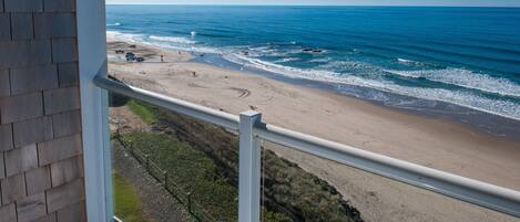 A beach view from a balcony with a railing, sandy beach, ocean waves, and a clear sky.