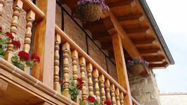 A wooden balcony with a stone wall, wooden balustrades, and flower baskets.