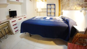 A bedroom with a bed, a desk, a chair, and a stone wall.