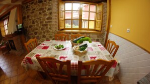 A dining area with a stone wall, a window with wooden shutters, and a table set with a checkered tablecloth and chairs.