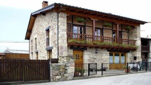 A stone building with a wooden balcony, a wooden fence, and a small garden area.
