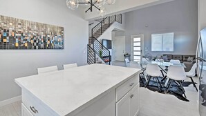 A modern kitchen with a large island, a dining area with white chairs, a staircase, and a living room with a sofa and a coffee table. - 7 Mi to Dtwn Phoenix: Group-Friendly Getaway (Phoenix)