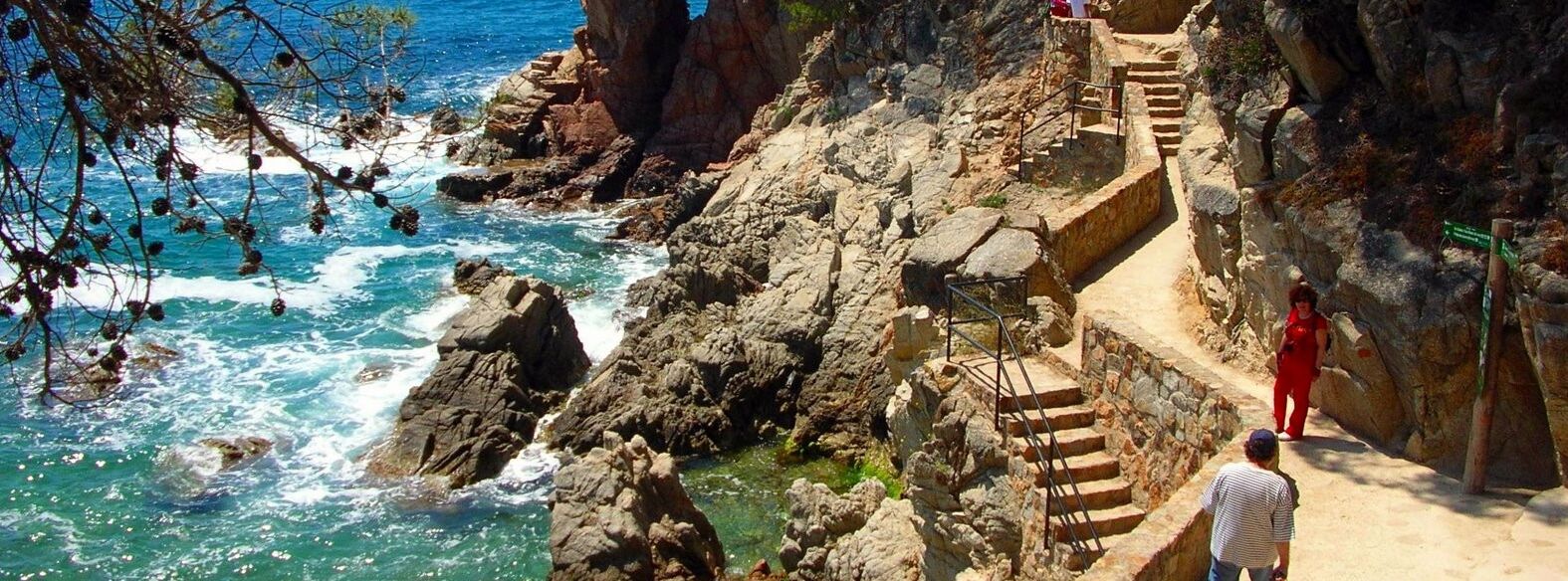 Une zone côtière rocheuse avec un escalier descendant jusqu'à la plage, d'où l'on a une vue sur la mer.