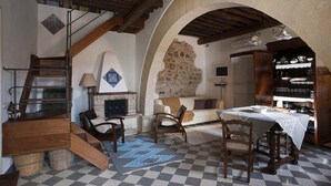 Une pièce rustique avec un mur en pierre, un escalier en bois, une cheminée, une table à manger et une bibliothèque.