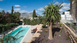 Un espace piscine offrant une vue sur les montagnes, entouré de verdure et bordé d’un mur de pierres.