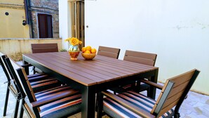 Une table à manger en bois, avec six chaises, un vase rempli de fleurs et un saladier d’oranges.
