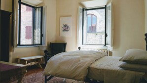 Une chambre à coucher avec un lit, une chaise, une table et deux fenêtres.
