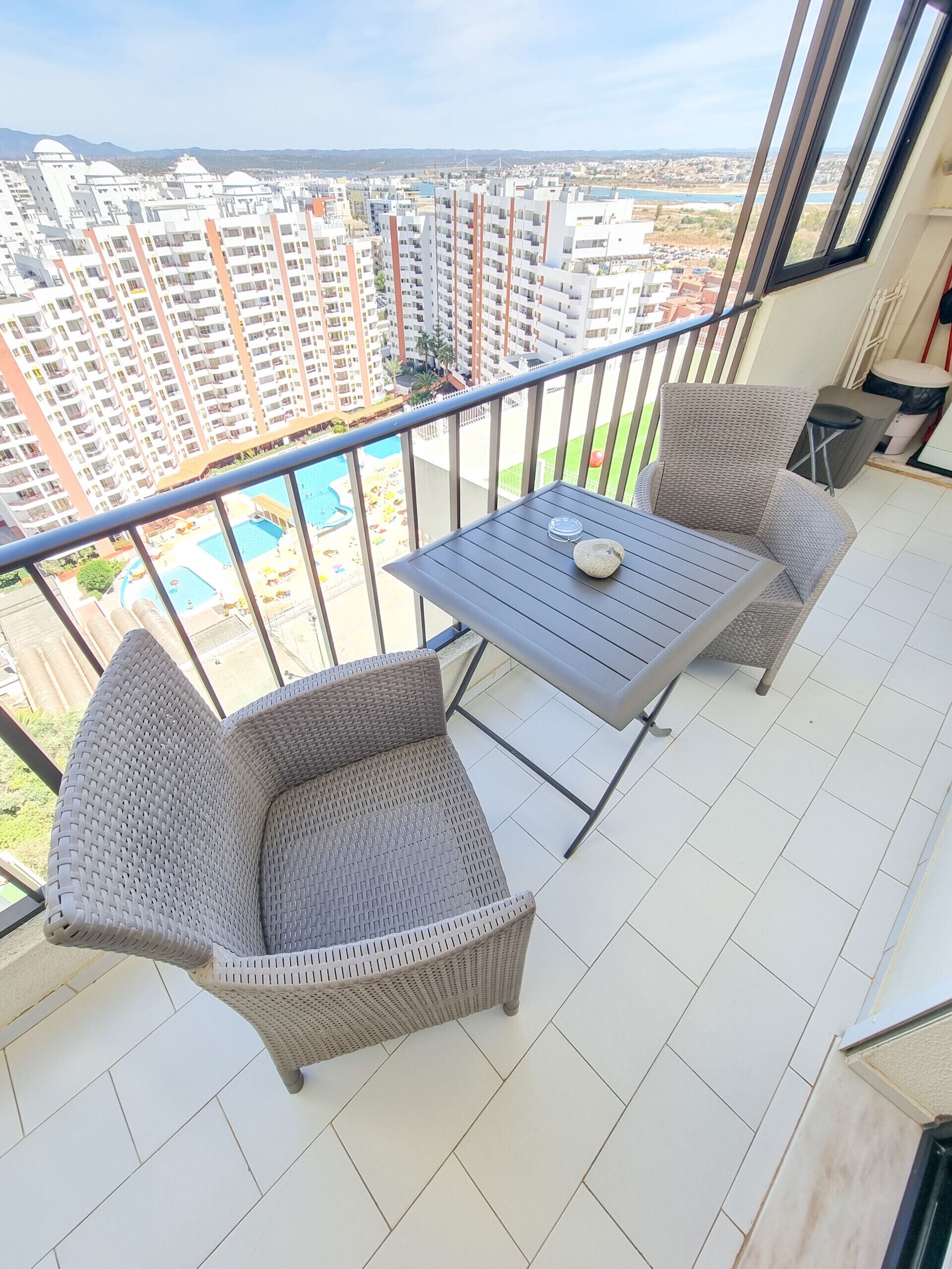 A balcony with wicker furniture and a view of a swimming pool and high-rise buildings.