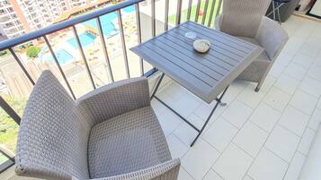 A balcony with wicker furniture and a view of a swimming pool and high-rise buildings.
