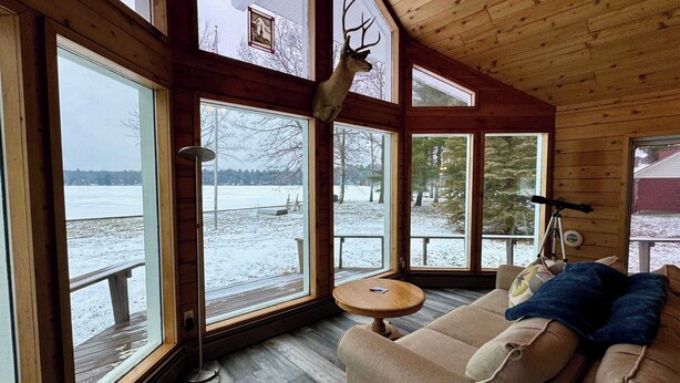 A cabin with large windows, a wooden ceiling, a sofa, and a deer head decoration. - Sandpiper Too | West Twin Lake Home (Lewiston)