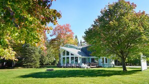 A house with a large glass front, a covered porch, and a lawn. - Sandpiper Too | West Twin Lake Home (Lewiston)