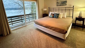 A bedroom with a large bed, a view of a lake, and a balcony. - Sandpiper Too | West Twin Lake Home (Lewiston)